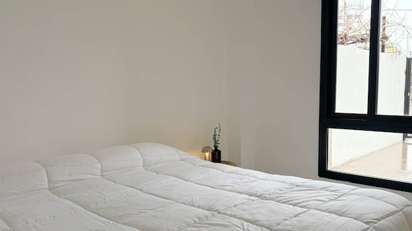 A bed with a white duvet in a room with a large window.