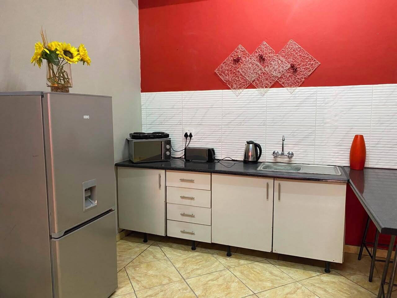 A compact kitchen with a refrigerator, microwave, toaster, sink, and a vase with flowers on the counter.