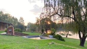 Zona verde con piscina, construcción de ladrillo y árboles.