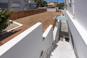 A residential area with a paved courtyard, a wooden fence, and a white building with a balcony. - Bright home 200m from the Beach (Porto Rafti)