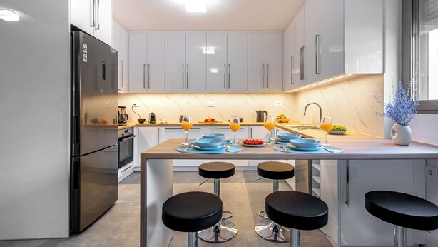A modern kitchen with a central island, bar stools, and a built-in oven. - Bright home 200m from the Beach (Porto Rafti)