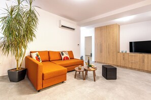 A modern living room with a sectional sofa, a potted plant, a small round table with drinks, and a TV in the background. - Bright home 200m from the Beach (Porto Rafti)