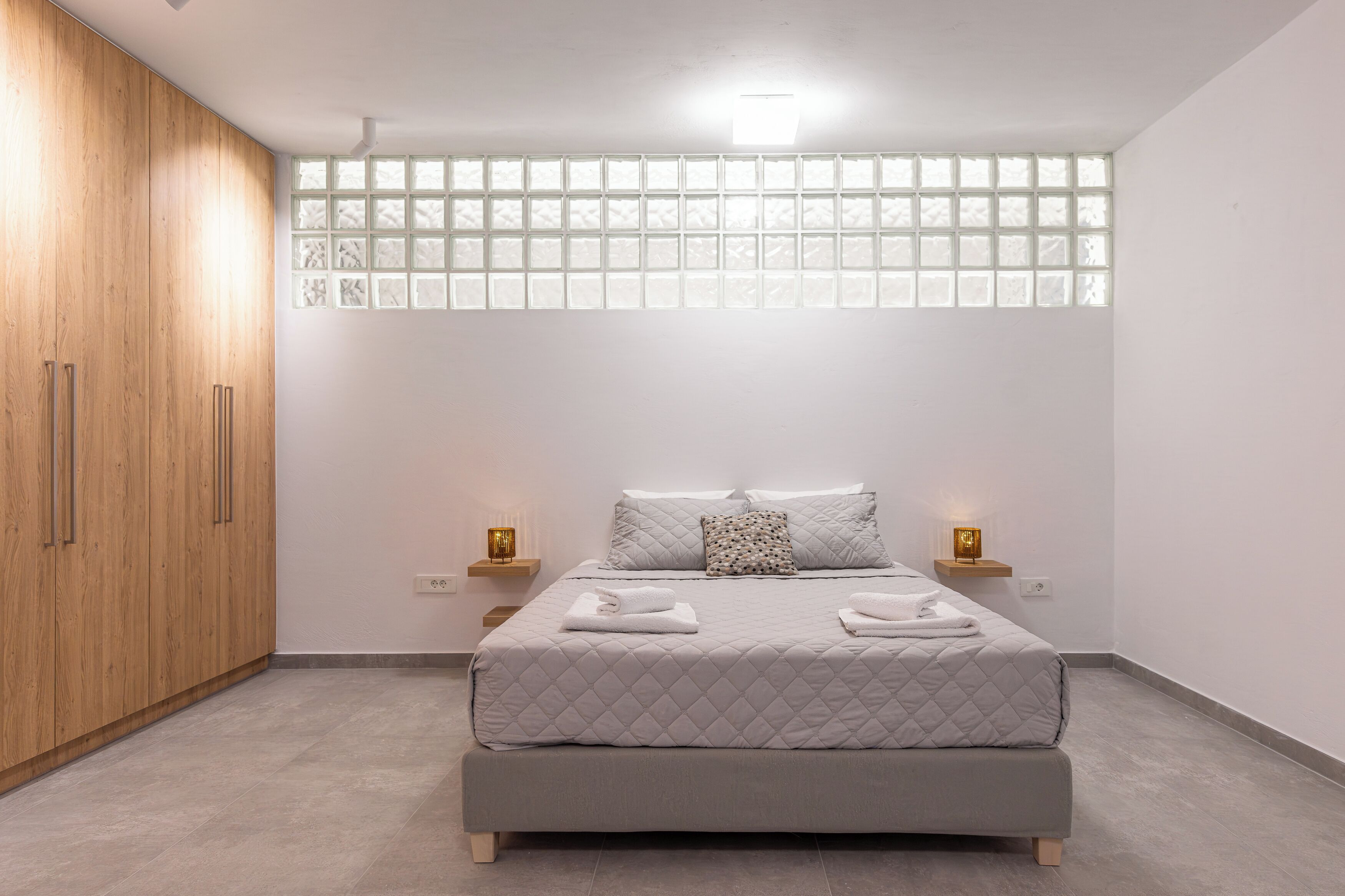 A bedroom with a bed, wooden wardrobe, bedside lamps, and a window with frosted glass panels.