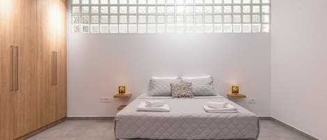A bedroom with a bed, wooden wardrobe, bedside lamps, and a window with frosted glass panels.