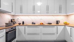 A modern kitchen with white cabinets, a marble backsplash, and a wooden countertop. - Bright home 200m from the Beach (Porto Rafti)