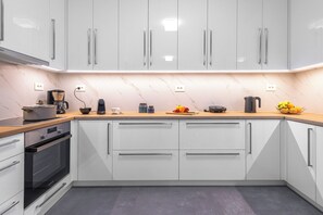 A modern kitchen with white cabinets, a marble backsplash, and a wooden countertop. - Bright home 200m from the Beach (Porto Rafti)