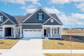 A two-story residential house with a garage, a covered front porch, and a well-maintained lawn.