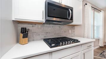 Una cocina moderna con armarios blancos, un microondas de acero inoxidable, una estufa a gas y un bloque para cuchillos.