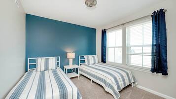 Un dormitorio con dos camas, una mesita de noche, una lámpara y una ventana con cortinas.