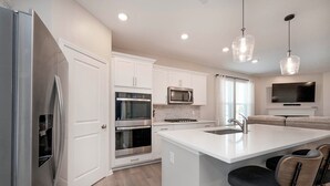 Una cocina moderna con armarios blancos, electrodomésticos de acero inoxidable, una isla grande con taburetes y luminarias colgantes.