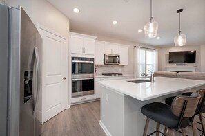 A modern kitchen with white cabinetry, stainless steel appliances, a large island with bar stools, and pendant lighting.