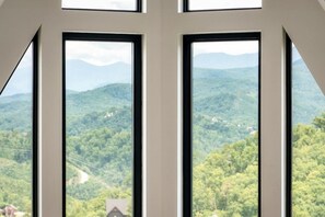 Ein Zimmer mit zwei großen Fenstern und Blick auf eine gebirgige Landschaft.