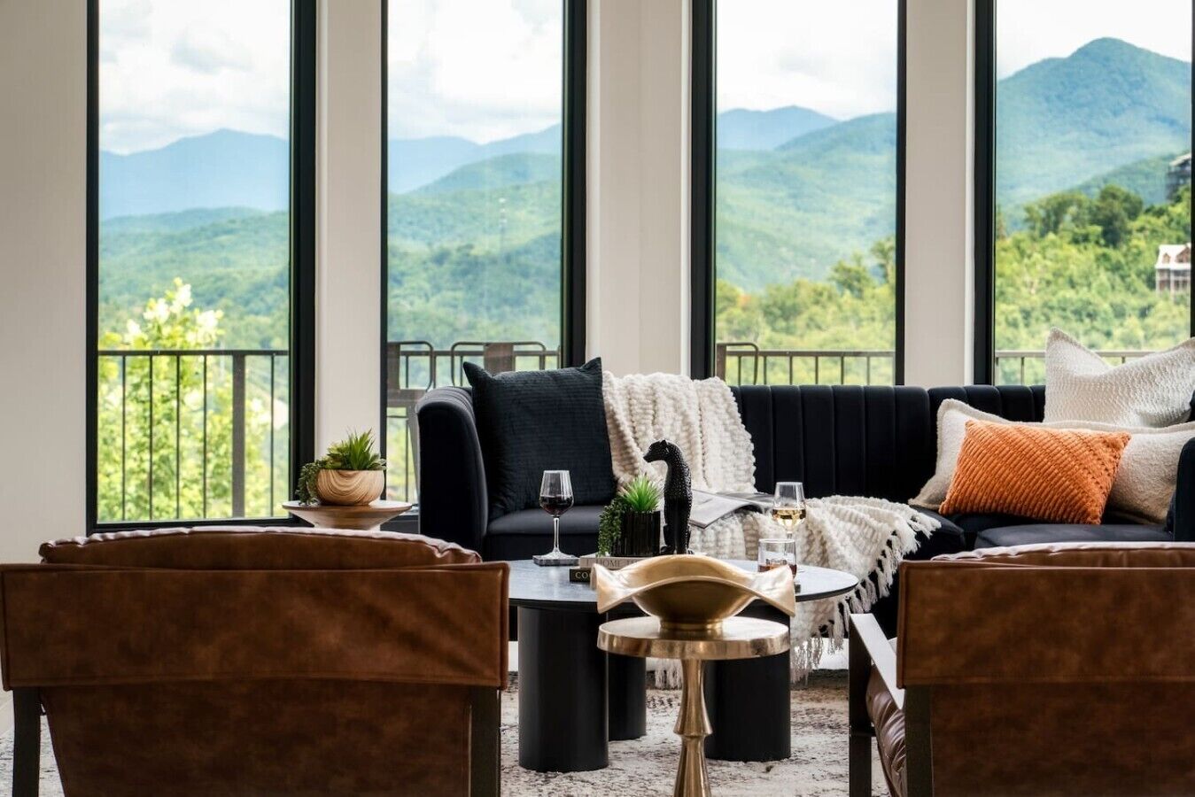 A cozy seating area with a sofa, chairs, and a coffee table, overlooking a mountainous landscape through large windows.