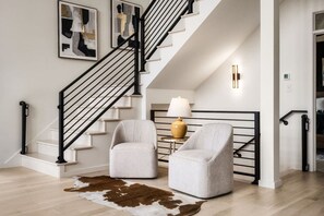 Eine Treppe mit schwarzen Geländern, zwei gepolsterte Sessel, eine Lampe und ein Kuhfellteppich.