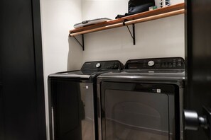 A laundry room with two front-loading washing machines and a wooden shelf above. - SwimSpa/HotTub/GameRoom/FirePit&Yard/Peloton/LUXE (Gatlinburg)