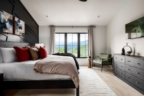 Ein Schlafzimmer mit einem großen Bett, einem Schminktisch, einem Sessel und Blick ins Freie.