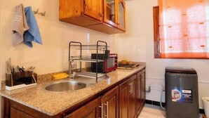 A kitchen with wooden cabinets, a stainless steel sink, a dish rack, and a trash bin. - Bright Apartment & Rooftop Terrace (Essaouira)