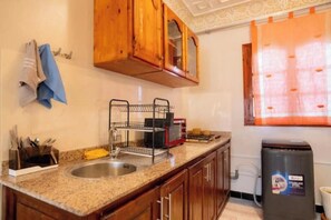 Uma cozinha com armários de madeira, pia de aço inoxidável, escorredor de louça e lixeira.
