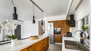 Una cocina moderna con una isla central, armarios de madera, electrodomésticos de acero inoxidable, iluminación colgante y vistas al área de comedor.