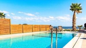 Una piscina con valla de madera, sillas de descanso y una palmera.