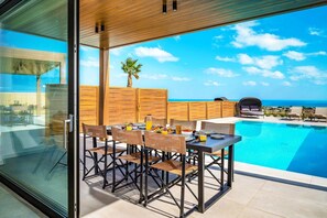 Ein moderner Essbereich im Freien mit Pool und Meerblick.