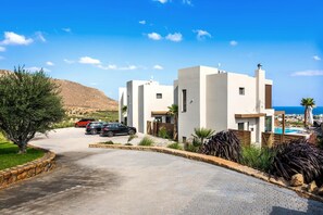 A modern building with a pool, parked cars, and a clear view of the sea. - Kamelia Luxury Villa 1 (Hersonissos)