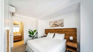 Un dormitorio moderno con una cama grande, cabecera de madera, mesitas de noche, una mesita auxiliar, una planta en maceta y un cuadro en la pared.