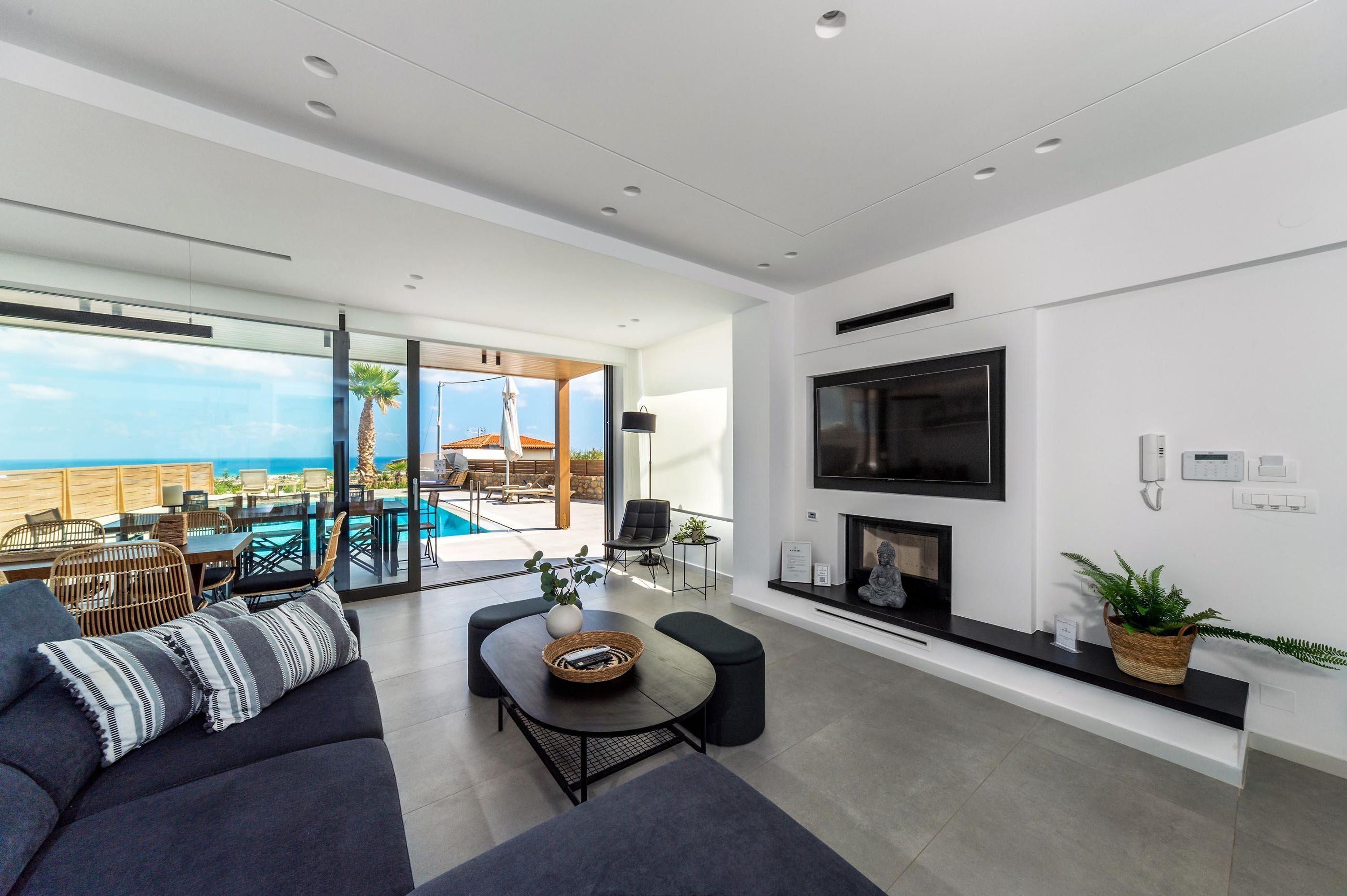 A modern living room with a large TV, fireplace, and a view of the pool and ocean.