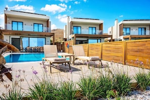 A modern outdoor pool area with lounge chairs and a wooden fence. - Kamelia Luxury Villa 1 (Hersonissos)