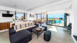 A modern living space with a kitchen, dining area, and a balcony with a pool view. - Kamelia Luxury Villa 2 (Hersonissos)