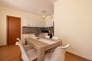 A dining area with a wooden table and four chairs, a kitchen with cabinets and appliances, and a wooden door. - Villa Melody in Zakynthos (Zakynthos)