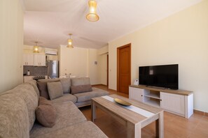 A modern living room with a sectional sofa, a coffee table, a flat-screen TV on a wooden stand, and a kitchen in the background. - Villa Melody in Zakynthos (Zakynthos)