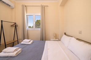 A hotel room with a bed, a nightstand, a lamp, a window with curtains, and a drying rack. - Villa Melody in Zakynthos (Zakynthos)