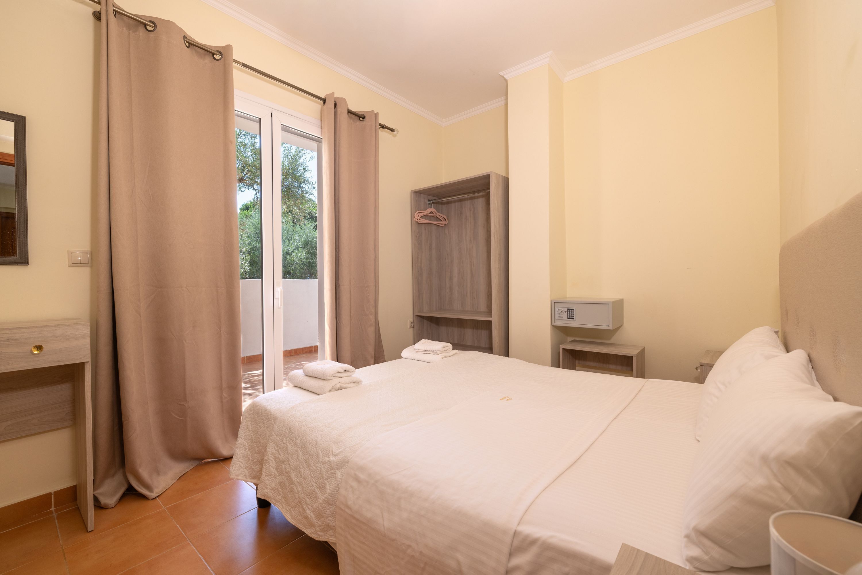 A hotel room with a bed, a bedside table, a nightstand, a wardrobe, and a view of the outdoors.