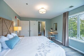 Ein Hotelzimmer mit Bett, Schreibtisch, Stuhl, Lampe, einem Vorhangfenster und einer Tür.