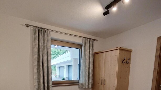 Ein Schlafzimmer mit zwei Betten, einem Holzschrank, einem Fenster mit Vorhängen und einer Deckenleuchte.