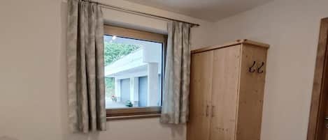 Un dormitorio con dos camas, un armario de madera, una ventana con cortinas y una lámpara en el techo.