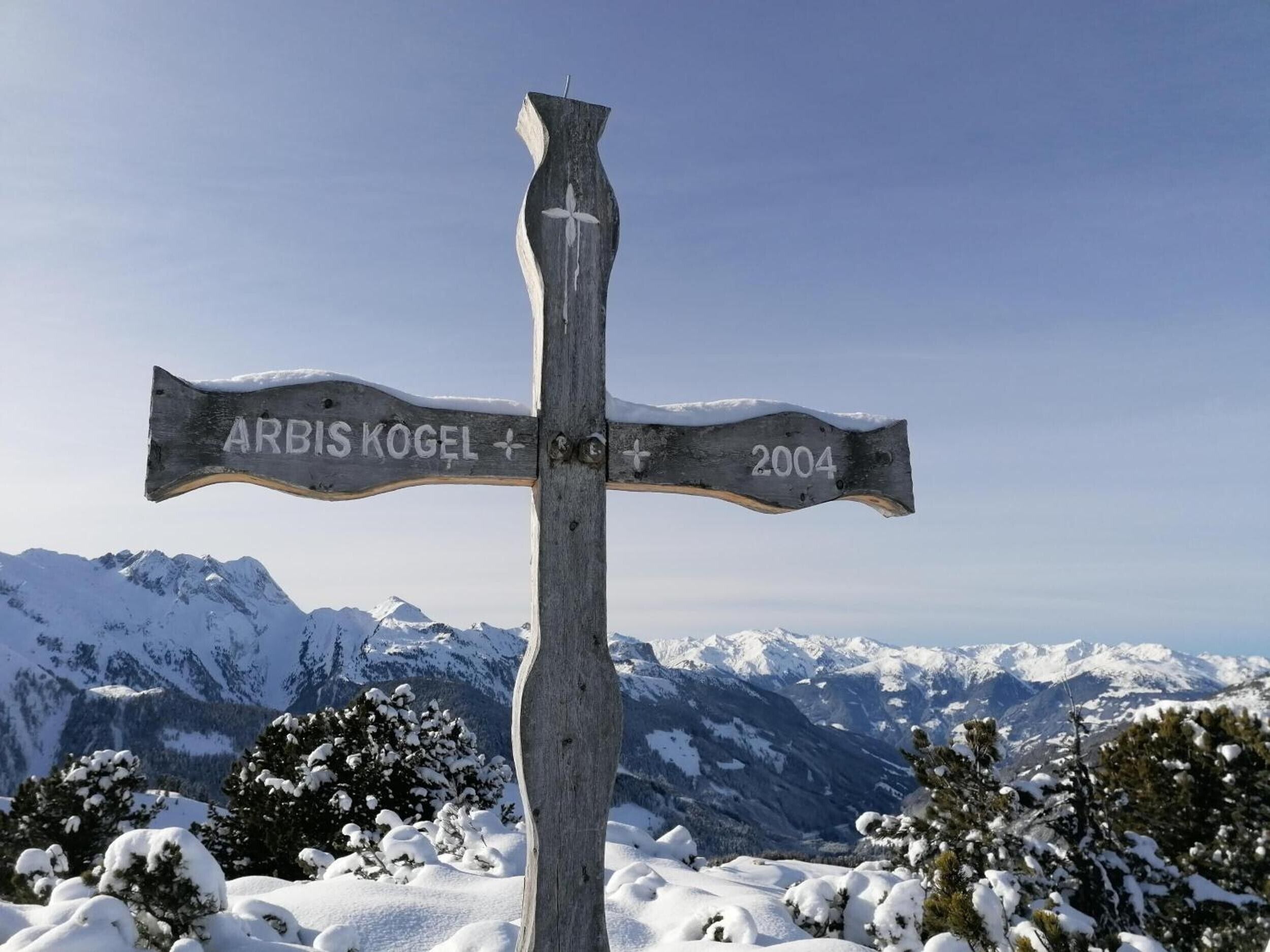Ein hölzernes Wegweiser mit Inschriften vor einer verschneiten Bergkulisse.