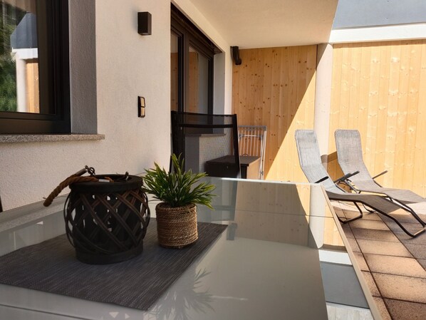 Una mesa de vidrio con una cesta tejida y una planta en maceta, una silla de metal y una valla de madera al fondo.
