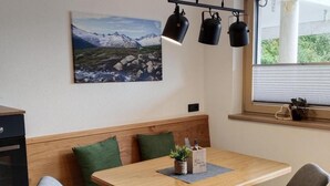 Eine moderne Küche mit Holztisch, zwei Stühlen, einer Bank und einem Fenster mit Blick ins Grüne.