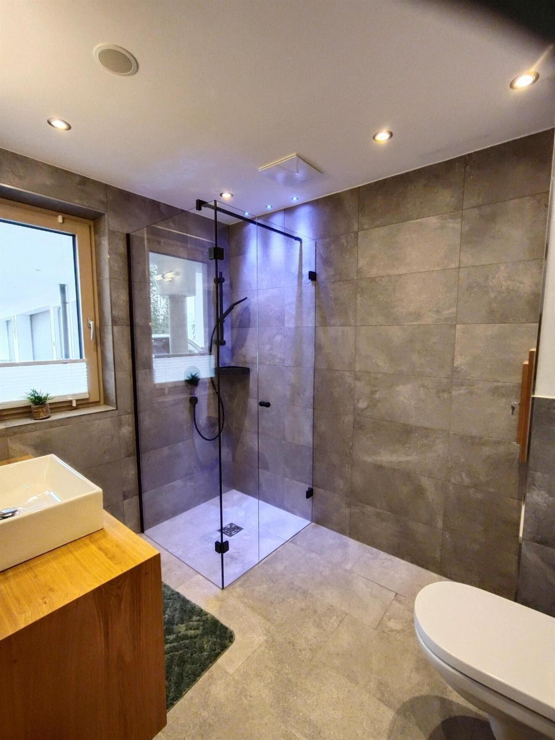 Ein modernes Badezimmer mit einer Duschkabine aus Glas, einer weißen Toilette und einem Holzausziehtisch.