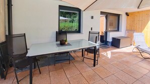 Ein überdachter Essbereich im Freien mit Tisch, Stühlen und Blick auf Grün durch ein Fenster.