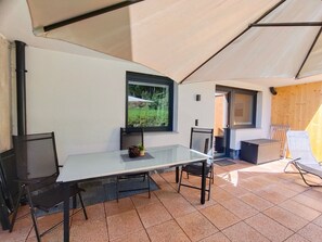 Un espacio de comedor techado al aire libre con una mesa, sillas y vistas a la vegetación a través de una ventana.