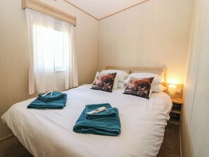Ein Hotelzimmer mit einem Bett, zwei Kissen, einem Nachttisch mit Lampe und einem Vorhangfenster.