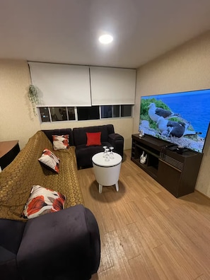 A living room with a sofa, a coffee table, and a flat-screen TV on a stand.