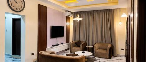 A modern living room with a sofa, two armchairs, a flat-screen TV, and a ceiling with geometric lighting.