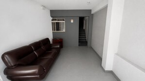 A hallway with a brown leather sofa, a small wooden table, and a staircase leading to another floor. - Aconchego de Lugar - Eri & Douglas - 3 (Belo Horizonte)
