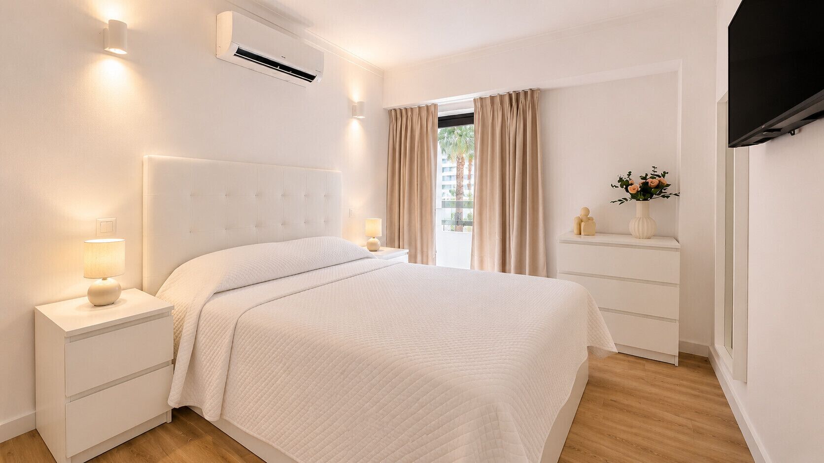 A bedroom with a bed, bedside tables, a nightstand, an air conditioning unit, a dresser, and a television.