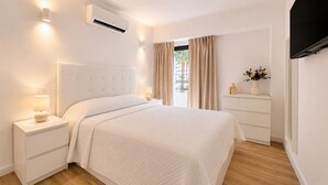 Een slaapkamer met een bed, nachtkastjes, een airconditioner, een dressoir en een televisie.