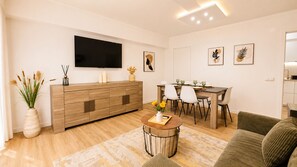 A modern living room with a wooden cabinet, a flat-screen TV, a dining table with chairs, and a sofa. - ATLANTIC BEACH APARTMENT (Quarteira)